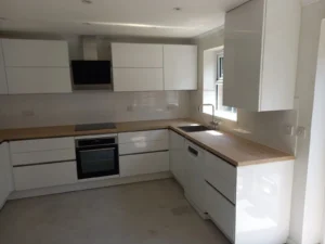 Kitchen with white cabinets, wooden worktop, oven, sink, wall sockets, and subway tile backsplash, with a window letting in natural light.