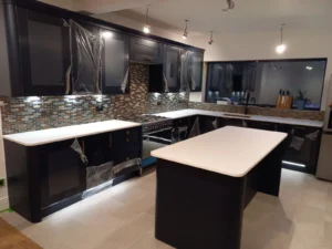 Kitchen with dark cabinets, white worktops, mosaic tile backsplash, central island, under-cabinet LED lighting, gas cooker, sink, and ceiling spotlights.