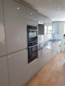 Sleek modern kitchen with glossy white cabinets, integrated appliances, subway tile backsplash, stainless steel sink, wooden floor, and black countertop.