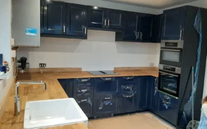 Kitchen with navy blue cabinets and wooden countertops, featuring a white sink and built-in appliances. Room is still under construction.