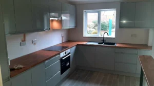 Kitchen with white cabinets, black sink, oven, wooden countertop, wall sockets, and a large window overlooking a garden.