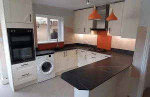 Kitchen featuring white cabinets, black worktops, a washing machine, cooker hood, gas stove, and orange pendant lights.