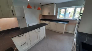 Kitchen with white cabinets, dark worktops, orange pendant lights, and a window showing greenery and parked cars.