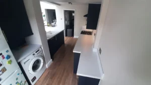 Kitchen with dark cabinets, white countertop, gas stove, washing machine, fridge, and wooden flooring.