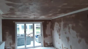 Partially renovated room with skimmed walls and ceiling, featuring large sliding doors opening into a conservatory.