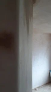 Partial view of a room with skimmed walls and partially visible floor, showing renovation debris.