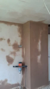 Partial view of a room with skimmed wall and ceiling, with a paint mixer leaning against the wall.