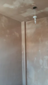 Partial view of a room with skimmed ceiling and walls, and a bulb holder hanging from the ceiling.